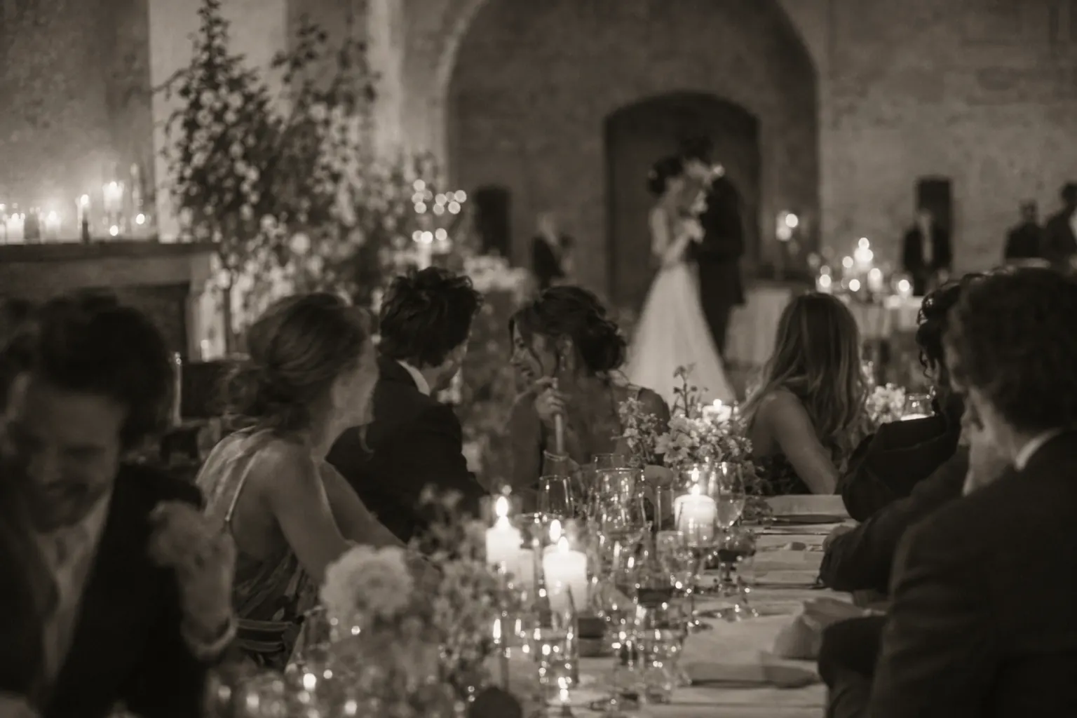 Black and white photograph of guests laughing around a long table late in the evening